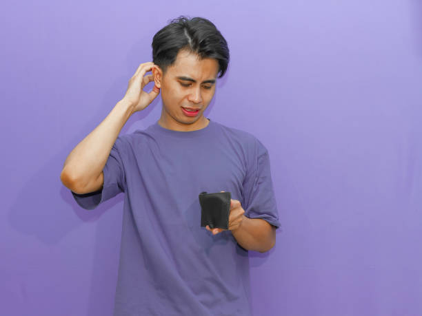 istock Poor young Asian man holds an empty wallet, showing a crying gesture on a purple background, highlighting financial struggles. 2182740112