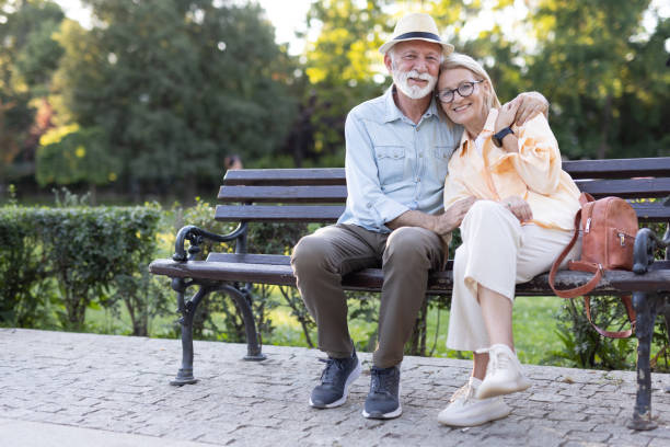 istock Happy elderly couple sitting closely on a park bench at daytime 2182743385