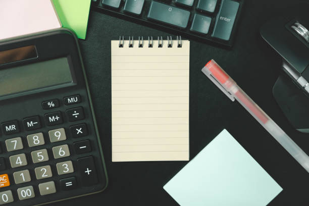 Top view of notebook. Blank paper notepad on office desk table with keyboard and other supplies. Blank notebook page for input the text. copy space, flat lay.
