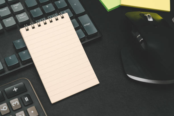 Top view of notebook. Blank paper notepad on office desk table with keyboard and other supplies. Blank notebook page for input the text. copy space, flat lay.