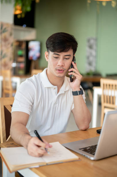 istock A focused Asian man is working remotely from a coffee shop, talking on the phone. 2182768933