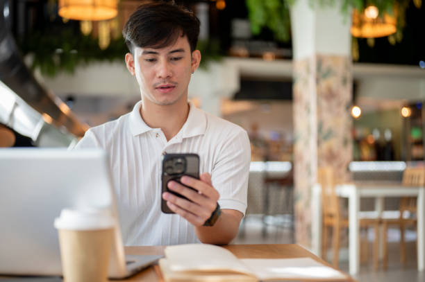 istock Handsome Asian man is focused on reading chat on his phone while working remotely from a coffee shop 2182769004