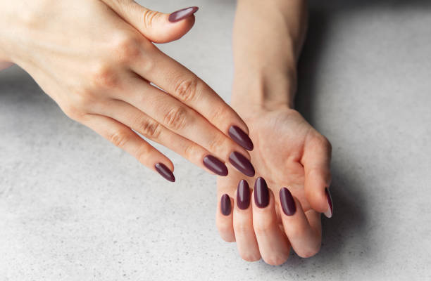 istock Elegant hands with almond-shaped maroon nails displayed against a gray tabletop background in soft lighting 2182778068