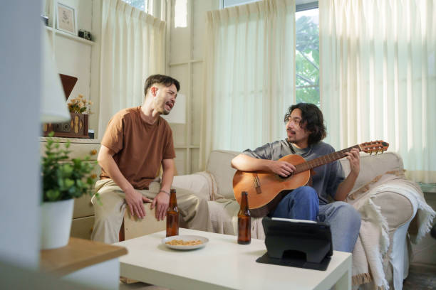 istock Asian playing guitar while his friend plays a cajon, both singing and enjoying a musical jam session in a living room. Friendship concept. 2182782926