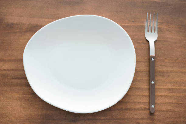 Empty white plate and fork on wooden background close up top view.