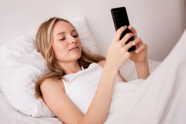 istock Young beautiful caucasian woman using smartphone in bed lying in bedroom spending weekend lazily 2182787892