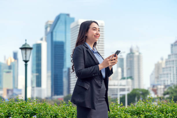 istock Asian Businesswoman Using Smartphone in Modern Urban Setting with Skyline Background 2182792185