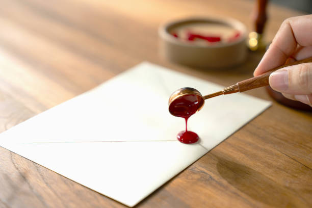 Dripping red wax onto a white envelope to seal it. resting on a rustic wooden table