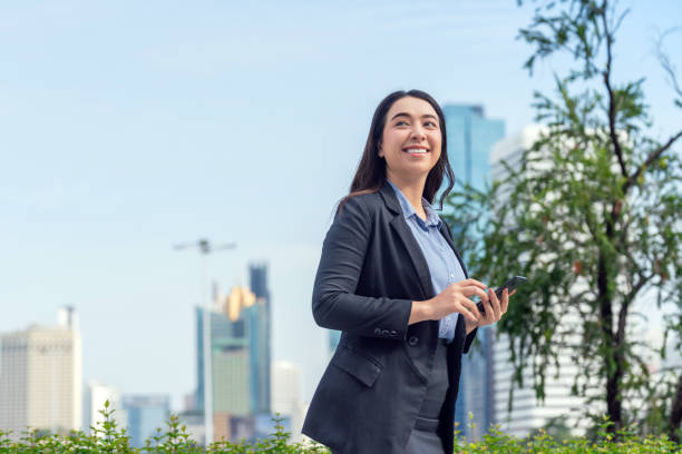 istock Asian Businesswoman Using Smartphone in Modern Urban Setting with Skyline Background 2182792324