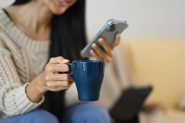 istock Smiling young woman enjoying a warm drink while checking messages on her mobile phone 2182795030