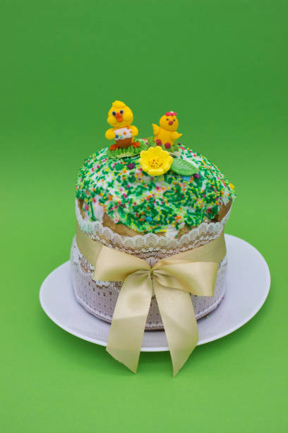 Easter cake with icing, colorful sprinkles, sugar figures, and a lace band with a yellow ribbon, placed on a green background. Perfect for holiday themes and festive celebrations