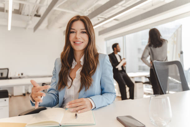 istock Smiling businesswoman gesturing while sitting at desk in office 2182808813