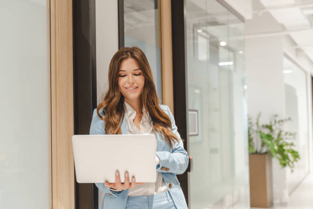 istock Smiling businesswoman using laptop in modern office corridor 2182808870