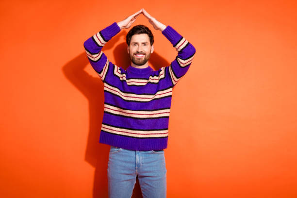 istock Confident man posing in striped sweater against vibrant orange backdrop, exuding modern style and fashion flair 2182809703