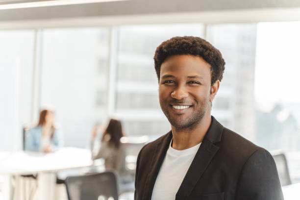 istock Smiling businessman standing in modern office with coworkers in background 2182811008