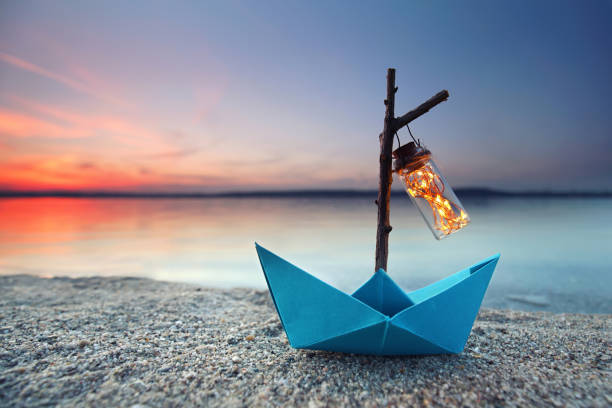 istock romantic evening - magical blue paper boat with lantern at the beach 2182816024