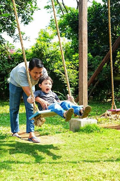 A joyful father pushes his excited son on a swing in a sunny garden. The child's wide-eyed expression captures the thrill and fun of the moment, while the father's smile radiates love and happiness.