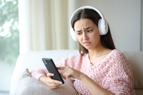 Disgusted woman checking phone using headphone stock photo