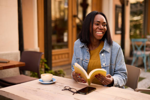 Woman is sitting in a cafe and enjoying her coffee while reading a book