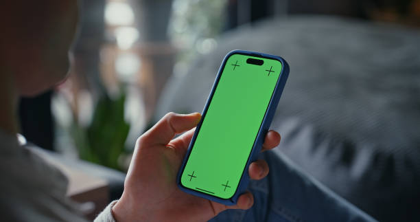 istock Person, hand and mobile with green screen for social media, connectivity or browsing internet in home. Network, man or phone on sofa for communication, news or streaming with display tracking markers 2182828784