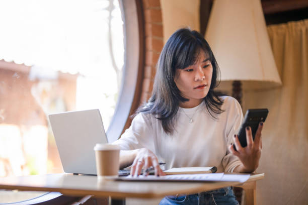 istock Cheerful Asian businesswoman multitasking with phone and documents while working from a sunny coffee shop 2182832096