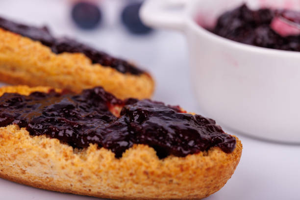 Unrecognizable young couple having jam on toast for breakfast, they are having a picnic and sitting on a blanket.