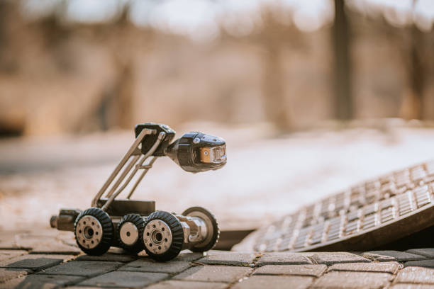 istock A small inspection robot with wheels and a camera is positioned near an open manhole, ready for underground exploration on a paved surface. 2182833373