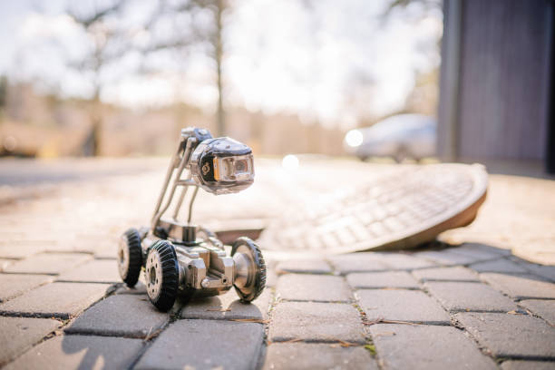 istock A small inspection robot with a camera on wheels is positioned on a cobblestone path near an open manhole, ready for underground exploration. 2182833386