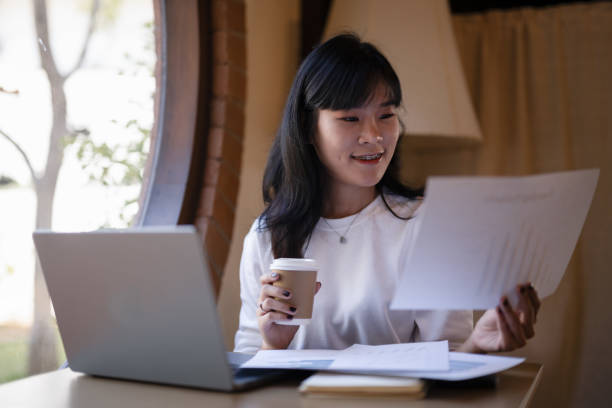 istock Young Asian woman enjoy with a coffee break while checking, reading documents in hand in a cafe. 2182833602