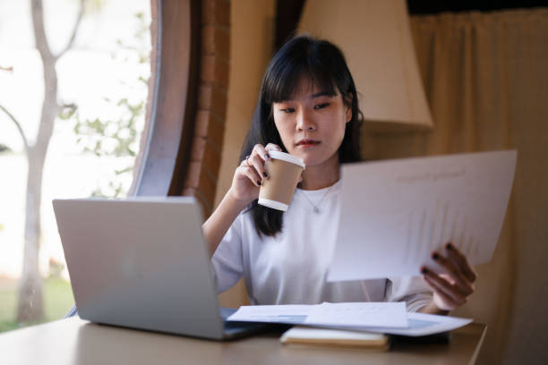 istock Young Asian woman enjoy with a coffee break while checking, reading documents in hand in a cafe. 2182833692