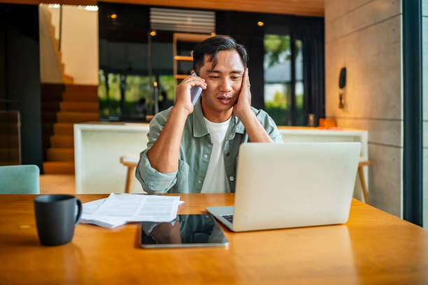 istock Young Man on Phone Call While Working Remotely at Home Office 2182833948