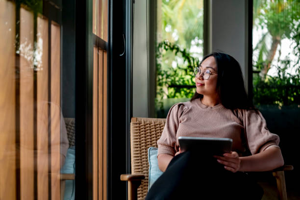istock Woman Relaxing Indoors by a Window with Tablet 2182833984