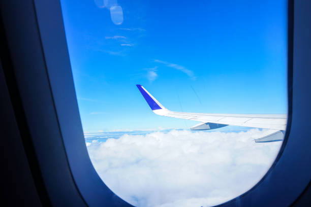 View of airplane wings from window against blue and cloudy sky. View from airplane window