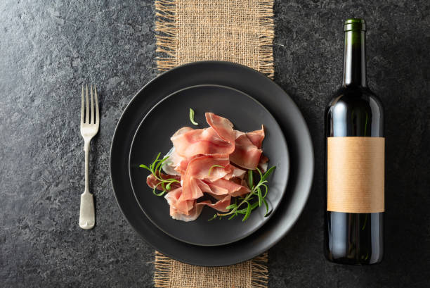 istock Bottle of red wine and prosciutto on a black plate. 2182841109