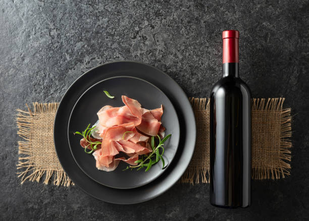 istock Bottle of red wine and prosciutto on a black plate. 2182841114