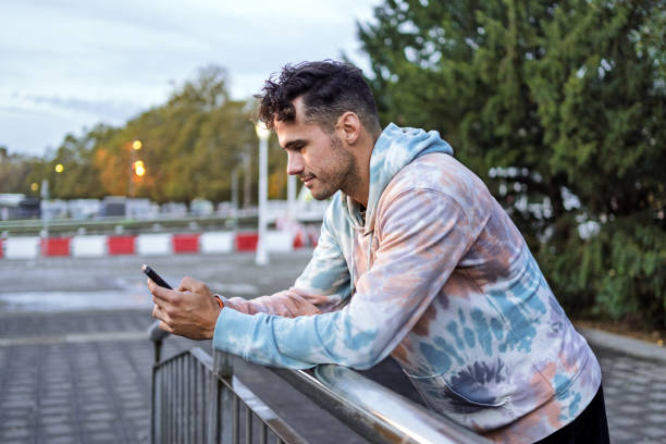 istock Fashionable man using smartphone while leaning on metal railing in city setting 2182844051