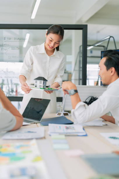 istock A woman presents house model during collaborative meeting, showcasing creativity and teamwork in modern office environment 2182849863