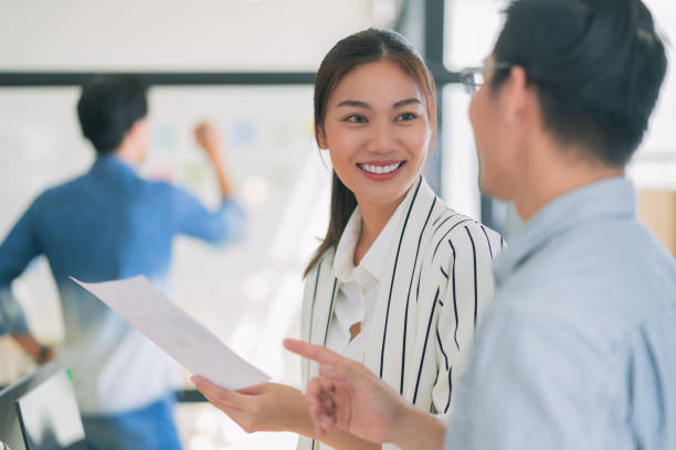 istock A professional woman smiles while discussing project with colleague in modern office setting. Their engaging conversation reflects teamwork and collaboration 2182850305