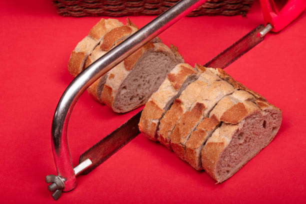 A creative and abstract presentation of sliced bread placed beneath a hacksaw on a red background, evoking themes of juxtaposition and uniqueness. Ideal for use in artistic, conceptual, or food-related projects needing a bold and unconventional image.