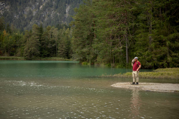 Handsome redhead senior man enjoying a moment of downtime at a lake during a forest bathing meditation trip in the Austrian Alps