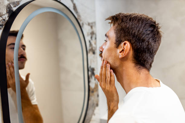 istock Man with a mustache applying face cream in bathroom in front of the mirror. 2182857575