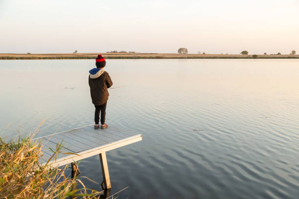 Rear view of a young boy fishing from a short dock on an early morning in autumn.