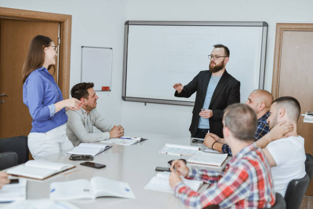 istock Male Professor Questioning Female Student in Class While Other Students are Listening 2182863103