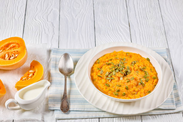 roasted butternut squash puree topped with pumpkin seeds in white bowl on white wooden table with spoon and ingredients, landscape view, free space