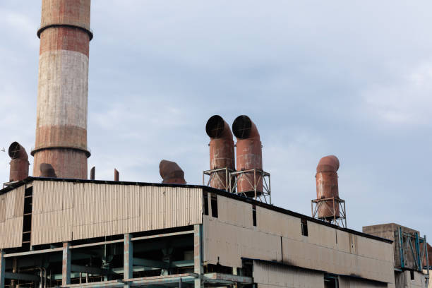 View of a thermal power plant boiler roof with safety valves and chimney in background on cloudy sky