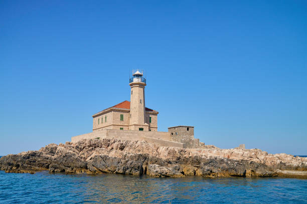 istock Seaside Lighthouse on Rocky Coast Under Clear Blue Sky 2182879159