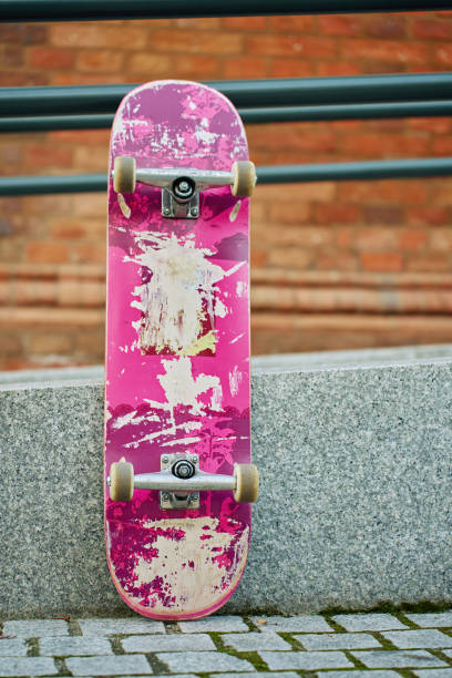 Used scratched pink skateboard against stone wall at city street. Urban sport and youth subculture concept