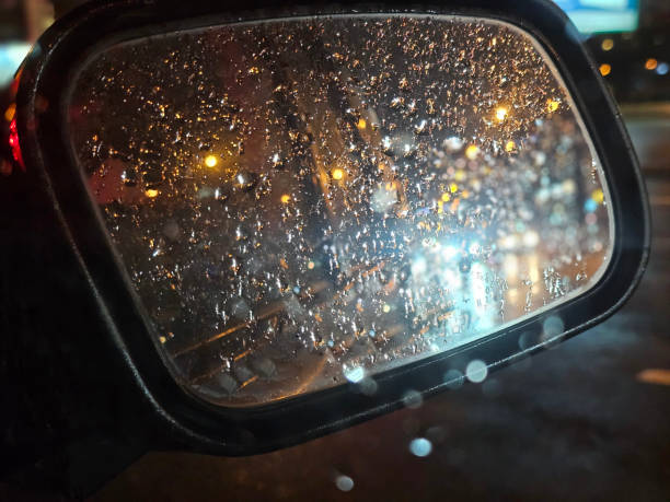 istock Raindrops on a side mirror reflecting city lights during a rainy night drive concept 2182881808