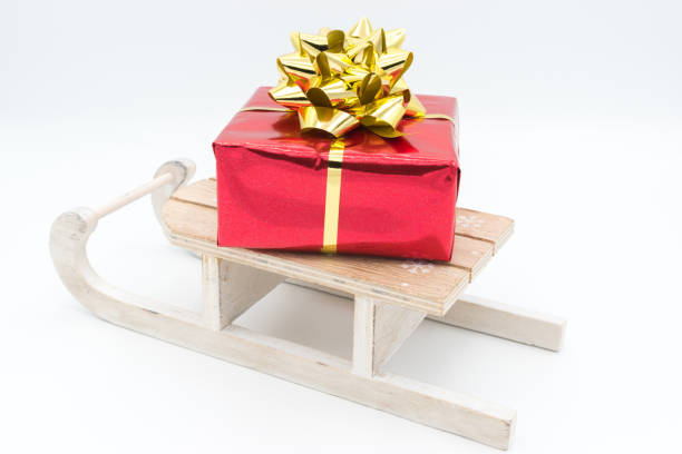 istock Red gift package with a golden ribbon, placed on a wooden sledge. 2182885722