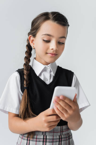istock A charming schoolgirl in her uniform joyfully engages with her smartphone in a studio setting 2182893016